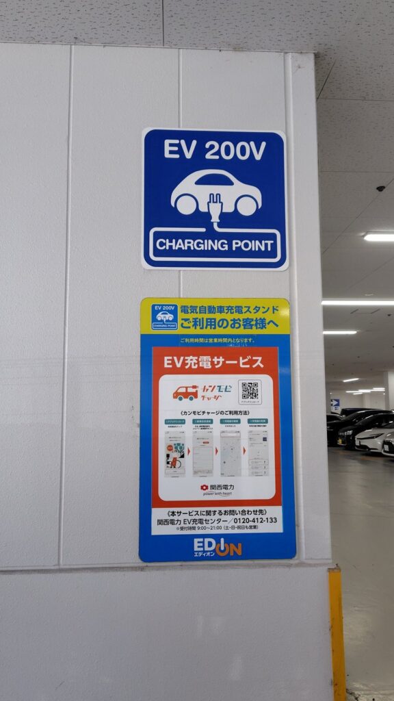 エディオンの駐車場にある「EV200V CHARGING POINT」の案内表示とカンモビチャージの利用案内